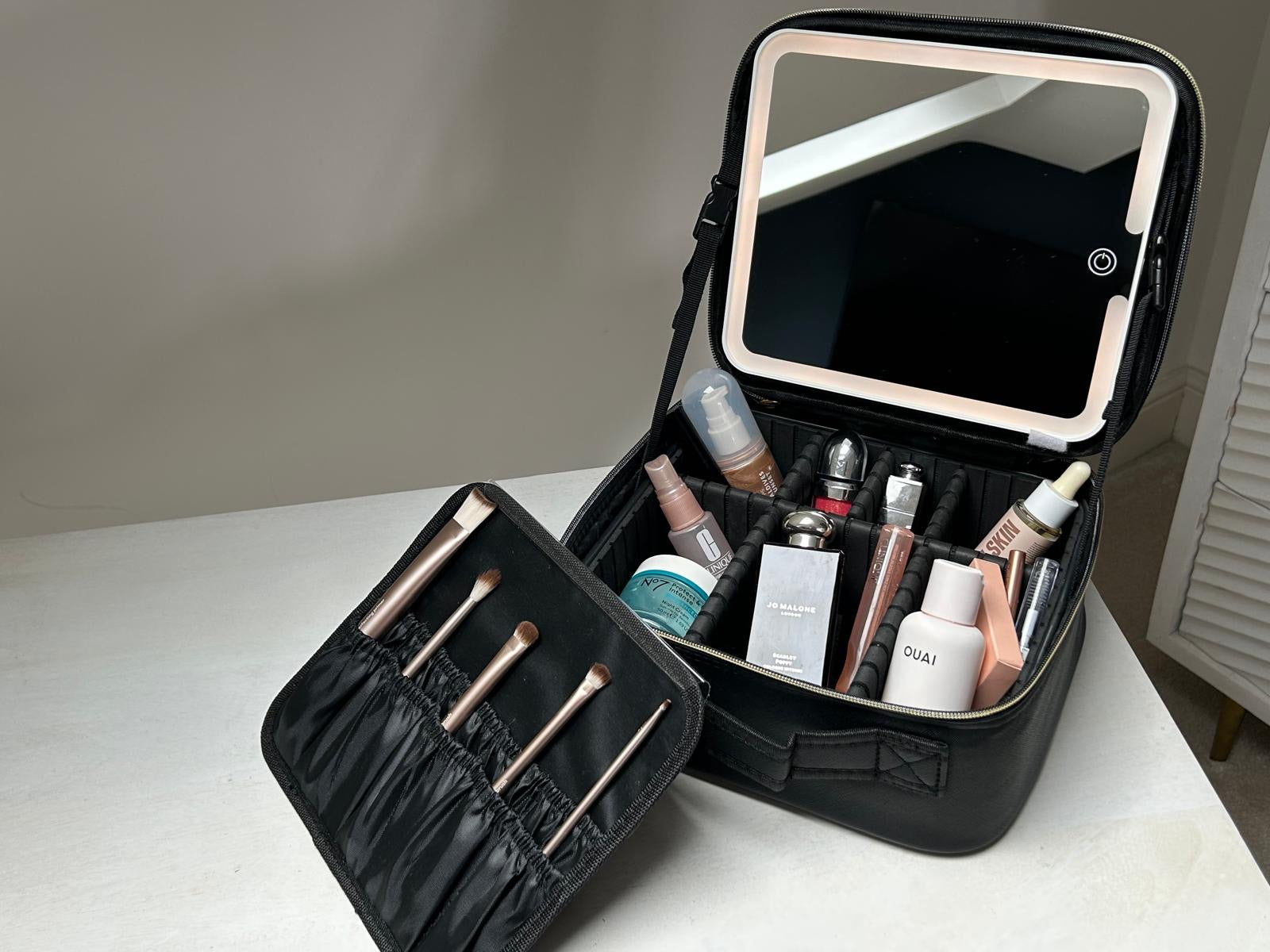 Black makeup travel case with mirror and cosmetic products on a white surface